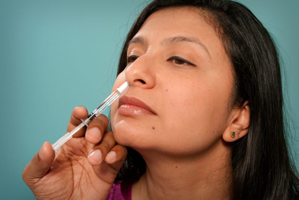 Woman receiving nasal injection near nose.